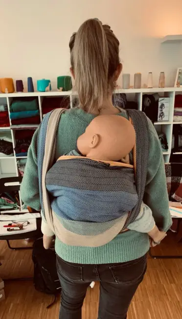 Isabel während einer Trageberatung in Tübingen mit einer Puppe im Rückentragetuch, zeigt sichere Binde-Techniken.